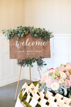 a welcome sign sitting on top of a table next to a basket filled with flowers