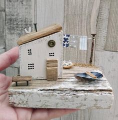 a miniature house made out of wood on top of a piece of driftwood with a blue and white flag