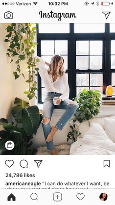 a woman sitting on top of a bed next to a window with plants in it