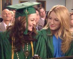 two women in green graduation gowns are smiling at the camera while others look on