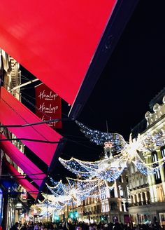 people are walking down the street in front of buildings with christmas lights hanging from them