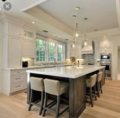 a large kitchen with an island in the middle and chairs around it, all white