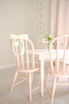 a white table and chairs with bows on the back, in a room that has pink walls