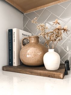 a white vase with flowers on a shelf next to a book and some other items