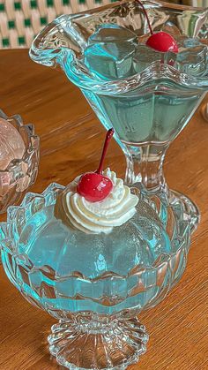 two glass dishes with ice cream and cherries in them sitting on a wooden table