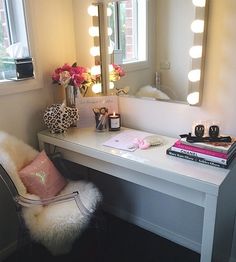 a white desk topped with a mirror next to a chair and a lamp on top of it