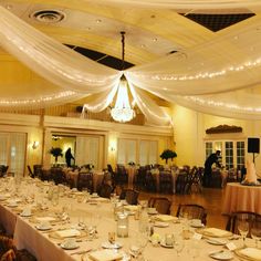 a banquet hall with tables and chairs covered in white draping over the ceiling