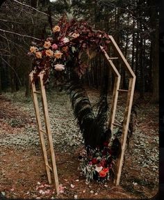 a wooden arch decorated with flowers and greenery stands in the middle of a forest