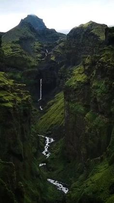 a man standing on top of a lush green hillside next to a tall cliff covered in grass