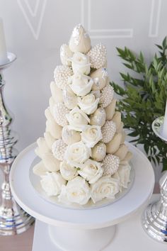 a white wedding cake decorated with flowers and seashells on a table next to potted plants