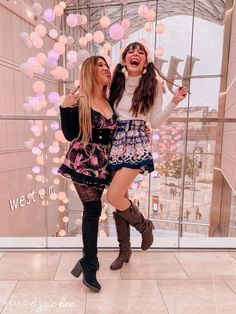 two young women standing next to each other in front of a glass wall with balloons