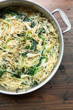 a pot filled with noodles and greens on top of a wooden table