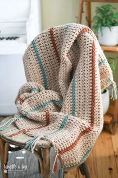 a crocheted blanket sitting on top of a wooden chair next to a potted plant