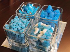 four clear containers filled with blue and white candies on top of a wooden table