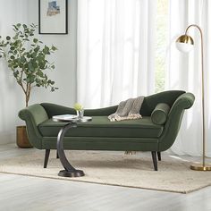 a green couch sitting on top of a white rug next to a table with a plant