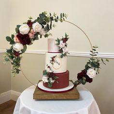 a wedding cake decorated with flowers and greenery on top of a wooden stand in front of a white wall