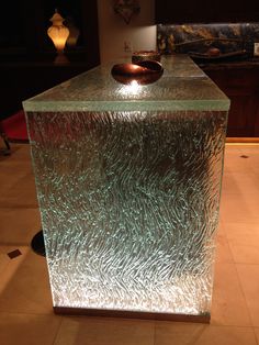 a shiny glass block with a bowl on it's top in the middle of a room