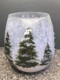 a glass with snow and trees painted on it sitting on a counter top next to a wall