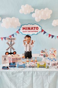 a little boy standing in front of a table filled with cakes and cupcakes