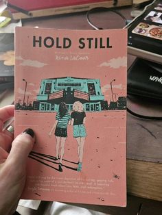 a person holding up a book about hold still