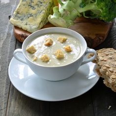 a bowl of soup on a saucer next to bread and broccoli with cheese