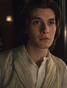 a young man with long hair wearing a white shirt and vest looking at the camera