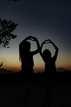 two people making heart shapes with their hands in the air at sunset or dawn time