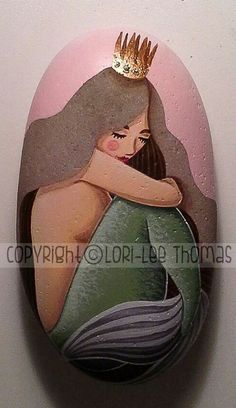 a painted rock with a woman wearing a tiara on it's head, sitting against a white wall