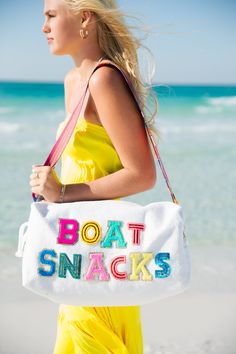 a woman carrying a white bag with the words boat snacks on it at the beach