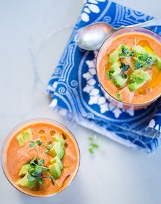 two bowls filled with soup and garnished with avocado on a blue towel