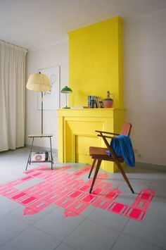 a chair sitting in front of a yellow fireplace with pink paint on the floor next to it