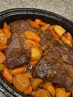 a pot roast with carrots and gravy in a black bowl on a counter