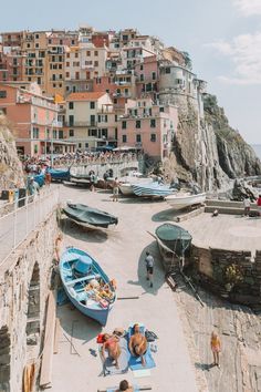 several boats are parked on the beach in front of some buildings and people walking around