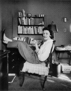 an old photo of a woman sitting at a desk in front of a bookshelf