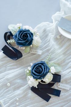 two blue and white flowers are sitting on a table with tags attached to the ribbons