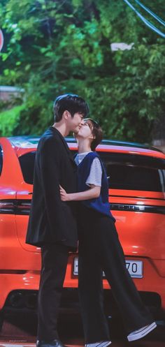 a man and woman kissing in front of an orange car