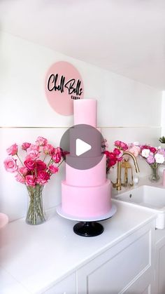 a pink cake sitting on top of a white counter next to vases with flowers