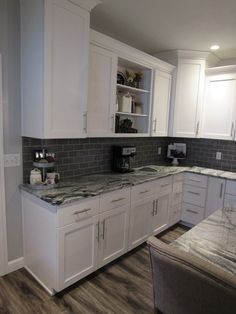 a kitchen with white cabinets and gray tile backsplash, granite counter tops and wooden flooring