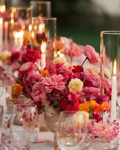 the table is set with pink and red flowers, candles, and glass vases