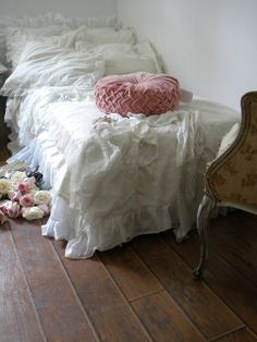 a white bed with ruffled bedspread and pink pillow on top of it