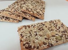 four pieces of food with seeds and nuts on them sitting on a white counter top