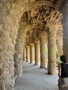 a woman is standing under an old stone structure