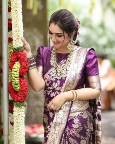 a woman in a purple and gold sari is placing flowers on a pole