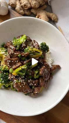 a white plate topped with beef and broccoli covered in sesame seeds on top of a wooden table