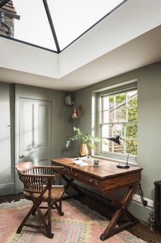 a room with a desk, chair and lamp on it in front of a window