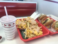 two trays filled with different types of food next to a cup of drink on a table