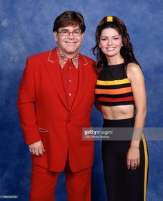 a man in a red suit standing next to a woman in a black and yellow top