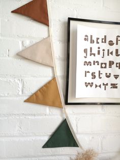 a white brick wall with three different colored triangles hanging from it's sides and a framed print on the wall