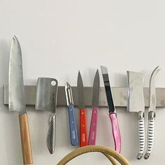 several knives are hanging on the wall with a basket in front of them and a knife holder next to it