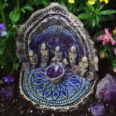 there is a small statue in the middle of some flowers and rocks with purple stones around it